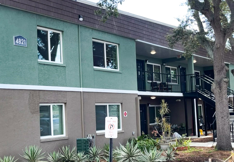 After: Two-story apartment building with a fresh two-tone exterior paint job—green on the upper section and brown on the lower half—accented by white trim and downspouts. The building has several white-framed windows.